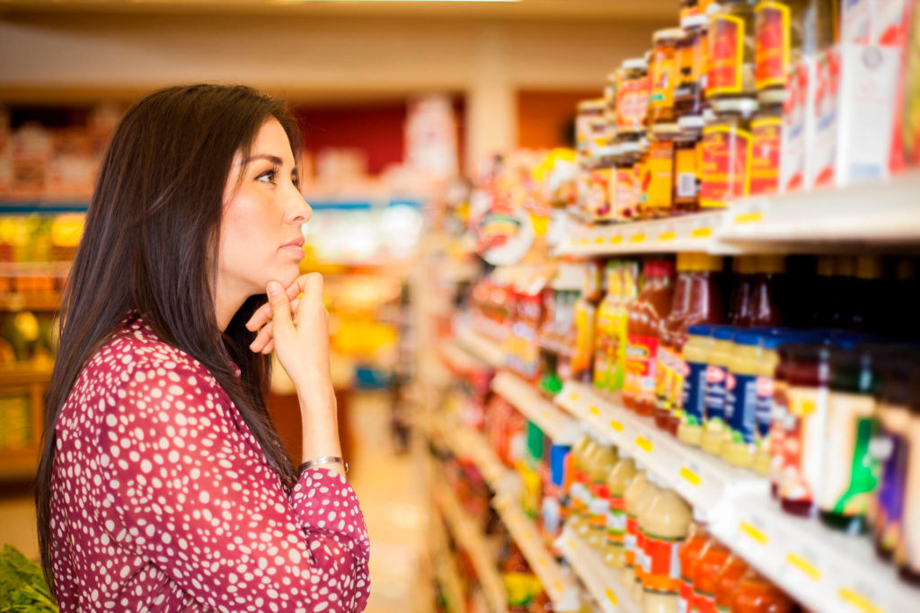Mulher em supermercado escolhendo produto na plateleira