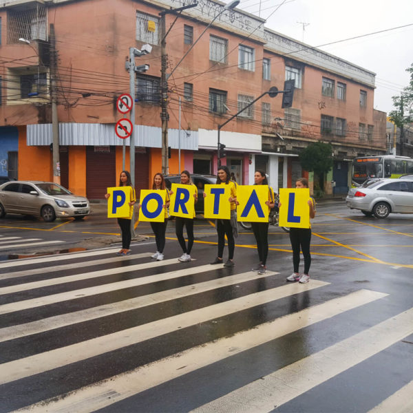 Promotoras segurando placa de letras formando a palavra "Portal"