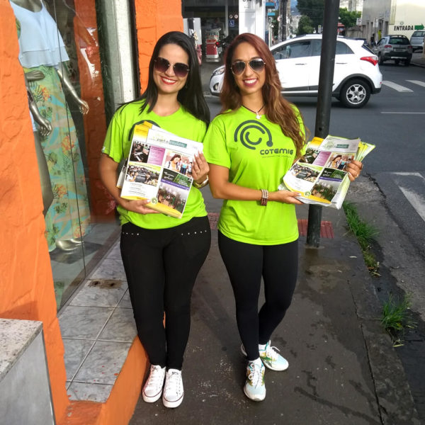 Duas promotoras do colégio Cotemig entregando jornal publicitário